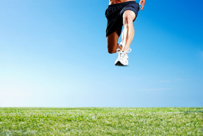 Low section of woman jumping on field against clear sky