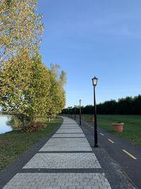 Street amidst trees against clear blue sky