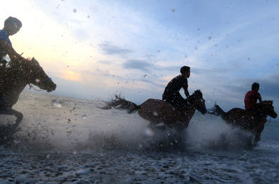 Men on wet shore against sky