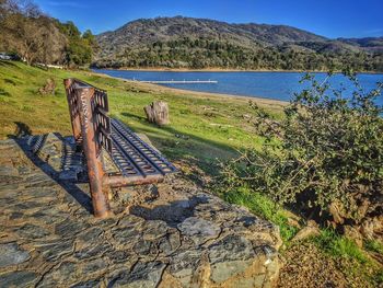 Scenic view of metal bench on stones against lake and mountains.