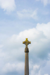 Low angle view of spire with christian cross  against cloudy sky