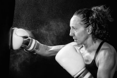 Female boxer punching bag against black background