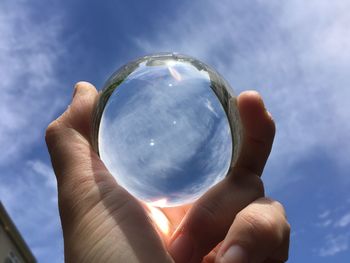 Close-up of hand holding crystal ball against blue sky