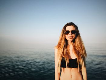 Beautiful woman in bikini standing at beach against clear sky on sunny day