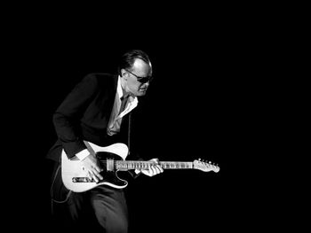 Man playing guitar against black background