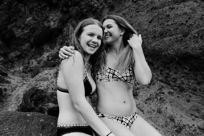 Happy female friends in bikini on rocky shore