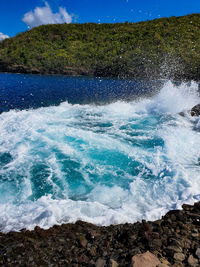 Waves splashing on shore against blue sky