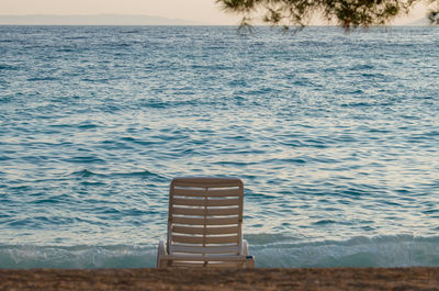 Chair on shore by sea against sky