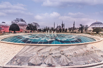 Fountain in park by building against sky