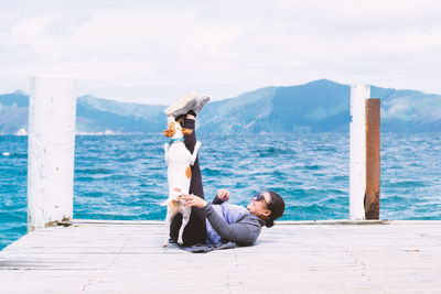 Side view of woman playing with her dog on a pier with blue sea and sky in background