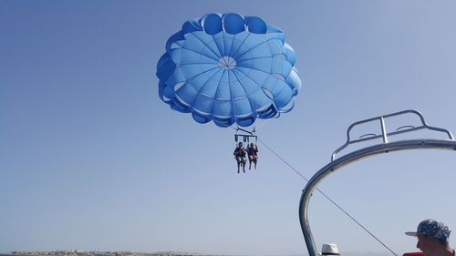 Low angle view of people paragliding against clear blue sky