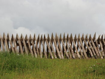 Sharp wooden fence on field against cloudy sky