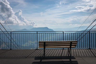 Empty bench by railing against sky