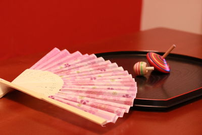 Close-up of pink folding fan with spinning tops on table