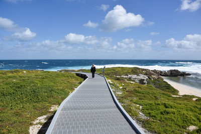 Woman standing on walkway by sea against sky