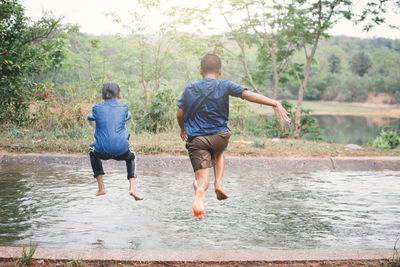 Siblings diving in lake against sky