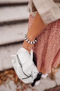 Black and white bracelet on woman hand and delicate suit skirt, jacket and student white backpack .