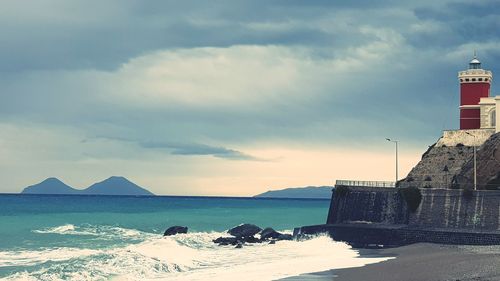 Lighthouse on beach by sea against sky