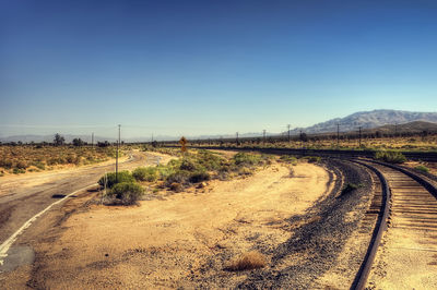 Road passing through field against clear sky