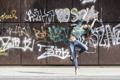 Full length of woman dancing against graffiti on wall