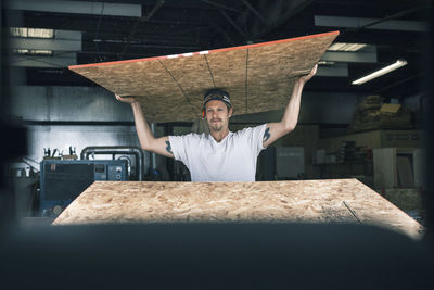 Carpenter carrying wooden plank on head at workshop