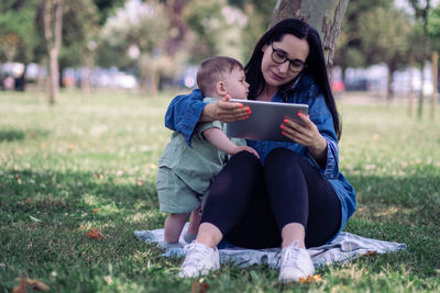 Young woman using phone while sitting on field