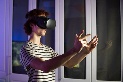 Young man wearing virtual reality simulator playing game at home