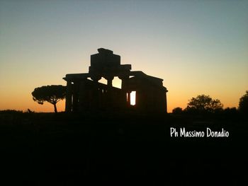 Silhouette built structure on field against clear sky at sunset