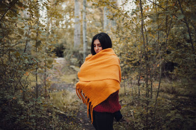 Woman dresses with her scarf inside the forest. autumn concept
