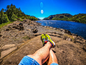 Low section of man on rock against blue sky