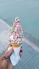 Cropped hand holding ice cream cone on street