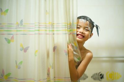 Portrait of smiling girl peeking from curtain while bathing at home