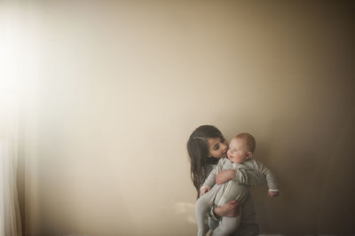 Sister carrying brother against wall at home