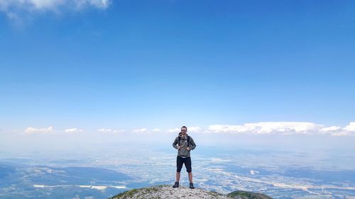 Full length of hiker standing on mountain against blue sky