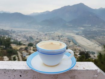 Close-up of coffee cup on railing against mountains