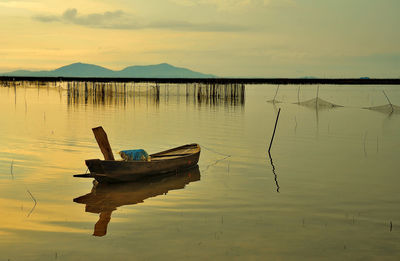 Boat moored in lake against sky during sunset
