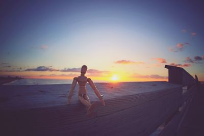 Wooden figurine on pier railing against sky during sunset