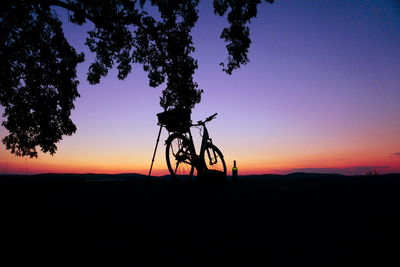 Silhouette bicycle on field against sky at sunset