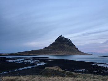 View of headland in calm sea against clouds