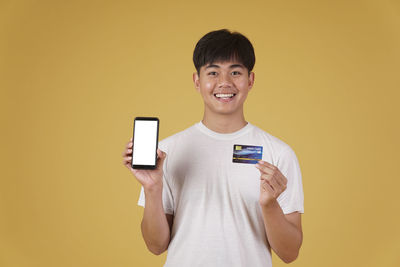 Portrait of smiling man holding camera while standing against orange background