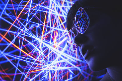 From below of female in trendy sunglasses illuminated by red and blue abstract neon lights in darkness