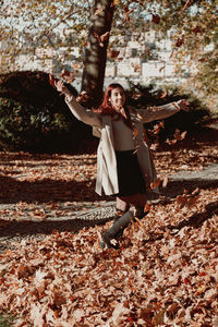 Full length of woman with arms raised on autumn leaves