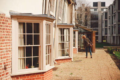 Rear view of woman standing on footpath by building