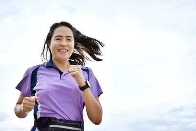 Portrait of smiling young woman running against sky