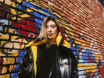 Portrait of young woman standing against brick wall