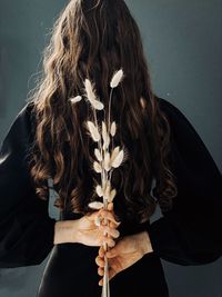 Rear view of woman holding flowers while standing against gray background