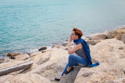 Side view of woman sitting on rock at beach