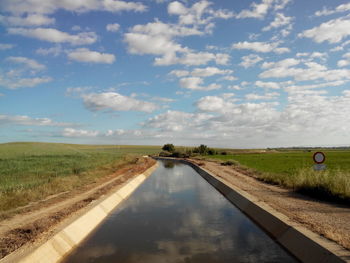 Road passing through field against cloudy sky