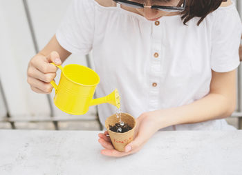 Caucasian teenage girl in a white shirt holds a yellow watering can with her hands
