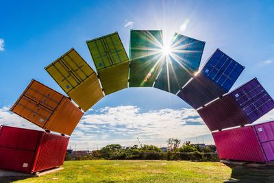 Multi colored cargo containers arranged in rainbow on field against sky during sunny day